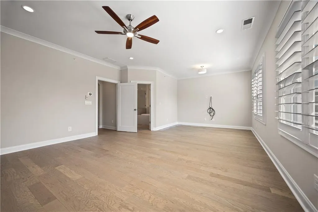 Primary bedroom with a ceiling fan, light wood-type flooring, baseboards, visible vents, and ornamental molding