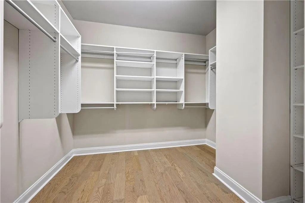Spacious primary closet featuring custom shelving and wood finished floors