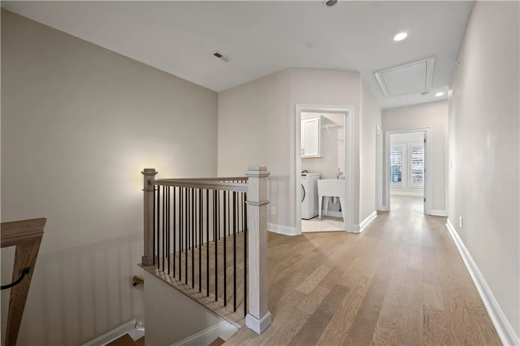 Hall with an upstairs landing, visible vents, light wood finished floors, washer / clothes dryer, and attic access