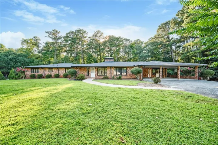 Brick ranch-style residence featuring a covered carport, expansive front lawn, and mature perimeter trees