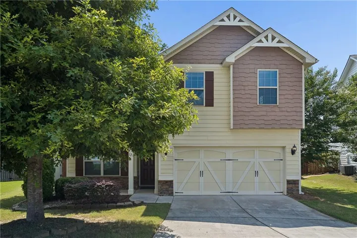 Two-story residence featuring light yellow siding, decorative gable vents, and a two-car garage with carriage-style doors