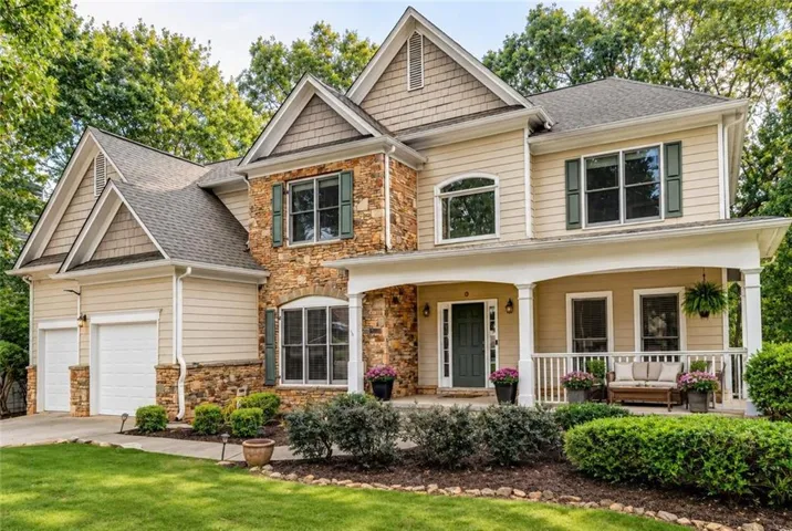 Stone and siding exterior with gabled roof lines, an inviting covered porch, a two-car garage, and established landscaping