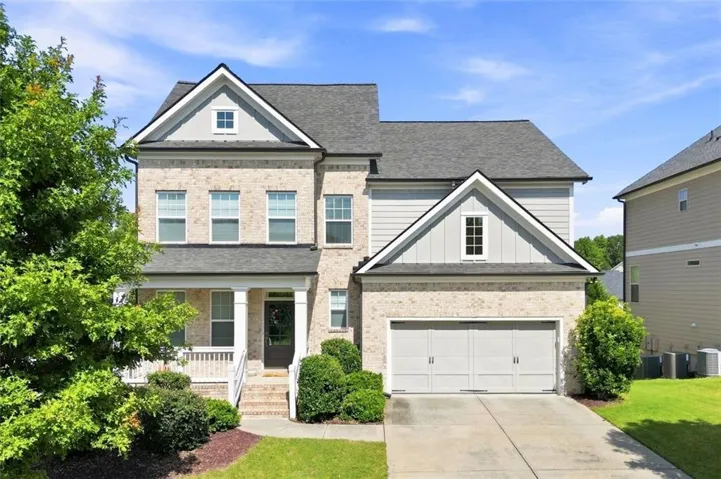 Brick and siding exterior featuring a covered front porch, two-car garage, and established landscaping