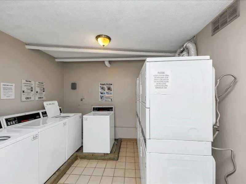 Common laundry area featuring light tile patterned floors, washing machine and dryer, visible vents, and a textured ceiling