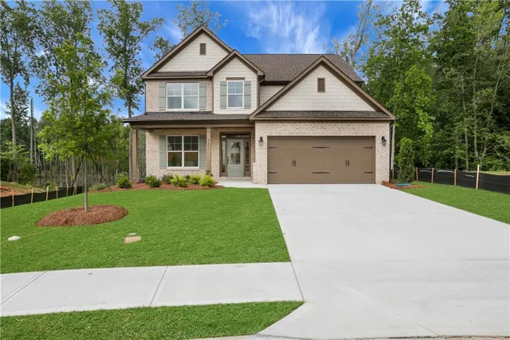 Stone veneer and siding exterior with a dark brown shingle roof, featuring an attached two-car garage with carriage-style doors, a concrete driveway, and a manicured lawn