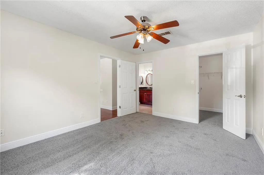 Unfurnished bedroom with carpet, a walk in closet, ensuite bathroom, and a ceiling fan