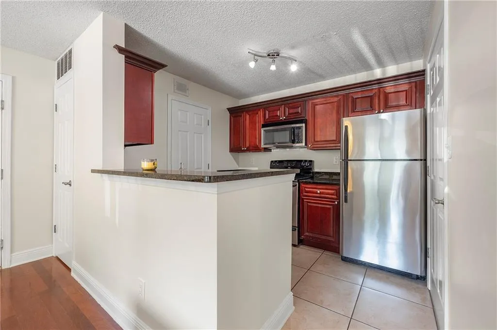 Kitchen featuring stainless steel appliances, dark brown cabinets, a peninsula, a textured ceiling, and light tile patterned flooring