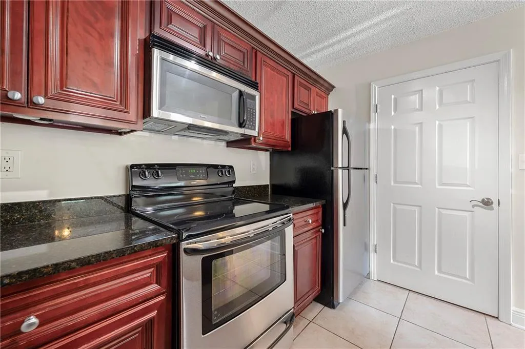 Kitchen with stainless steel appliances, dark brown cabinets, light tile patterned floors, dark stone counters, and a textured ceiling