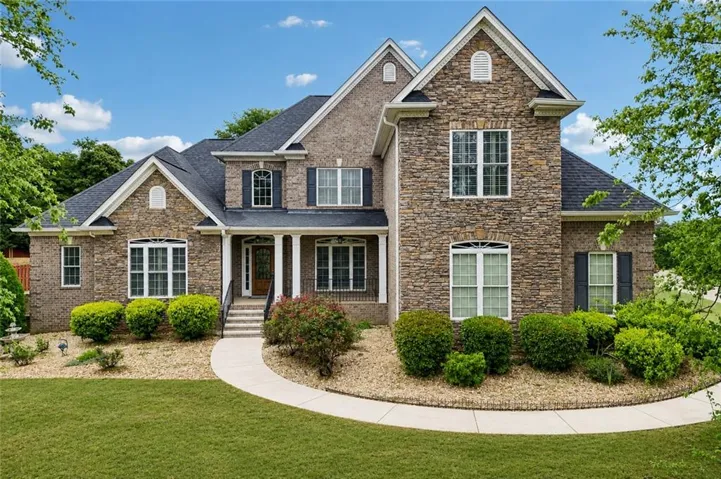 Stone and brick facade with dark shingle roof, complemented by a covered front entry with white columns