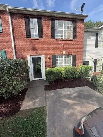 Two-story brick facade featuring multiple windows with black shutters, a white framed entry door, and a concrete pathway
