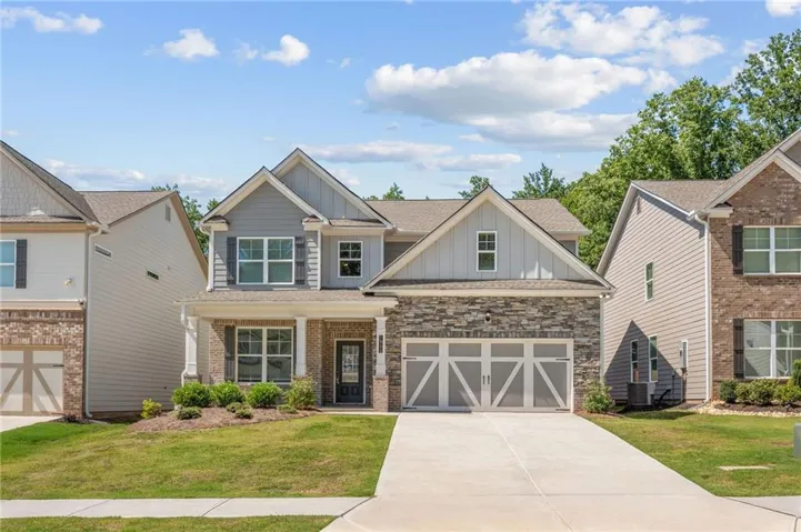 Two-story home with a stone and siding facade, covered front porch, and a two-car garage with decorative doors