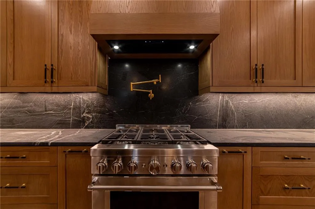 Kitchen featuring stainless steel range, tasteful backsplash, brown cabinets, and ventilation hood