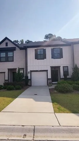 Two-story townhome featuring board and batten siding, dark framed windows, and a concrete driveway