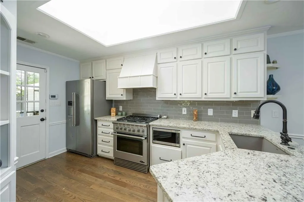 Kitchen featuring dark wood-type flooring, high quality appliances, white cabinetry, custom range hood, and light stone countertops