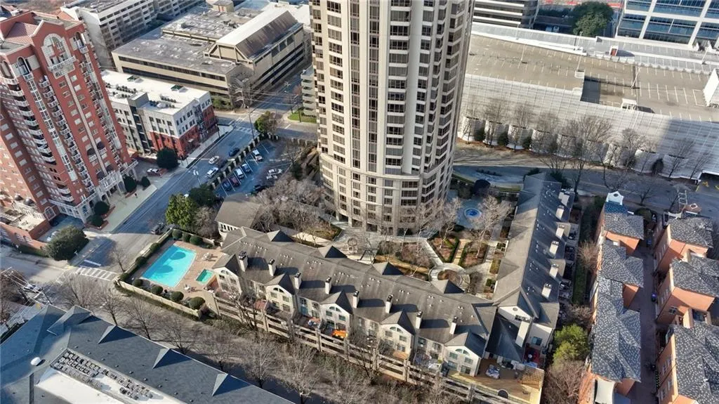 Elevated perspective showcasing a residential complex featuring a central high-rise building, a row of townhomes, and an outdoor swimming pool