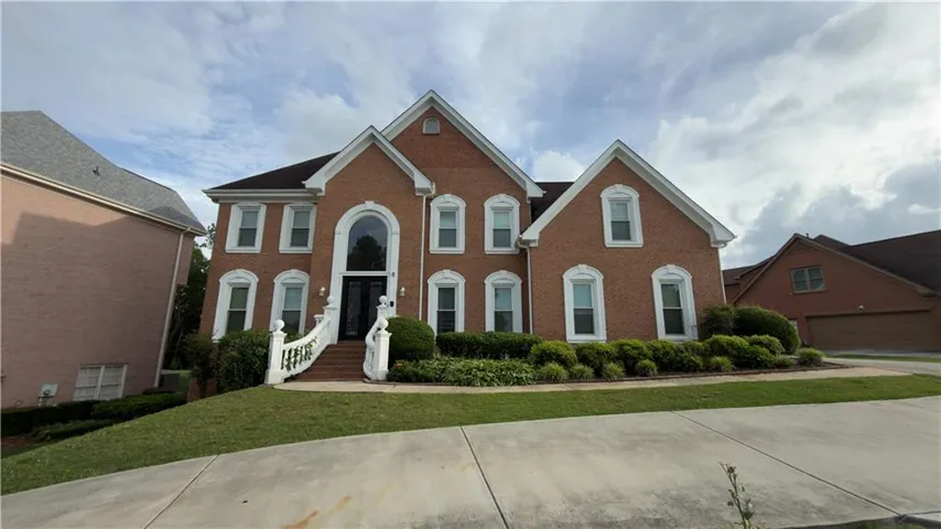Brick exterior residence with a prominent arched window above double entry doors, a curved staircase with white balustrade, mature landscaping, and a multi-car garage