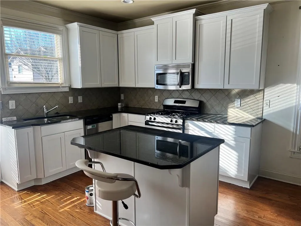 Kitchen with sink, white cabinetry, wood-type flooring, and stainless steel appliances