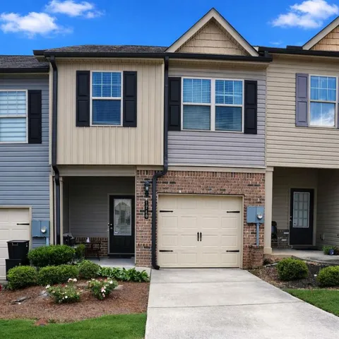 Two-story townhome featuring a neutral-toned garage door, brick facade detailing, and dark window shutters
