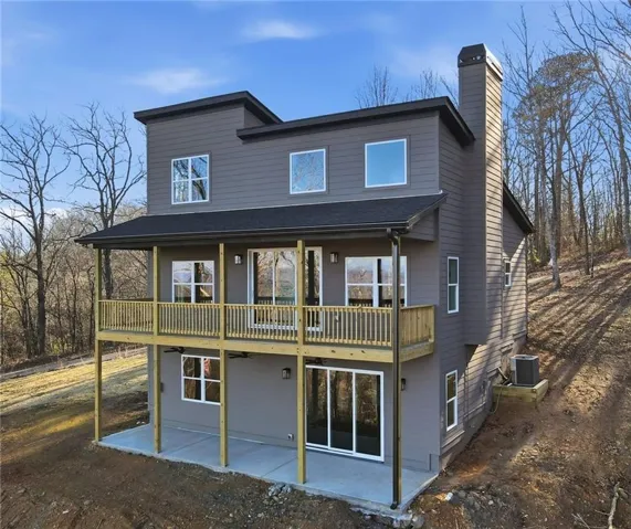 Modern three-story exterior with dark gray siding, an expansive upper-level deck, and a lower-level concrete patio