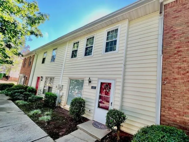 Contemporary townhome featuring horizontal vinyl siding, multiple double-hung windows with dark trim, a welcoming entry door with sidelights, and mature landscaping with boxwood plantings along the foundation