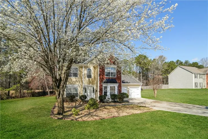 Two-story residence with a prominent mature tree, attached two-car garage, and a concrete driveway