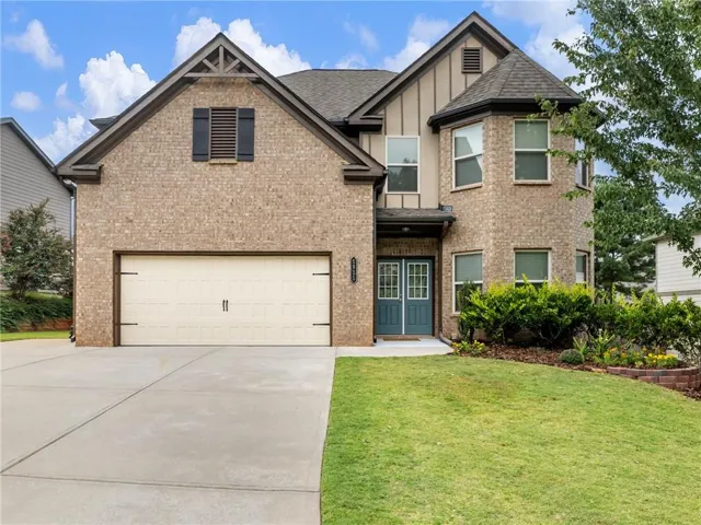 Brick facade with stone accents, two-car garage, turret architectural feature, double entry doors, and mature landscaping