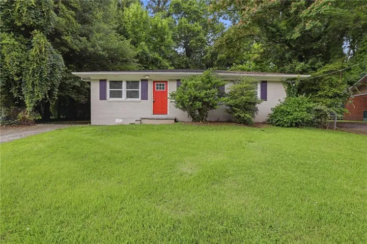 Single-story residence featuring a light gray brick exterior, a vibrant red entry door with grid detailing, and purple decorative shutters
