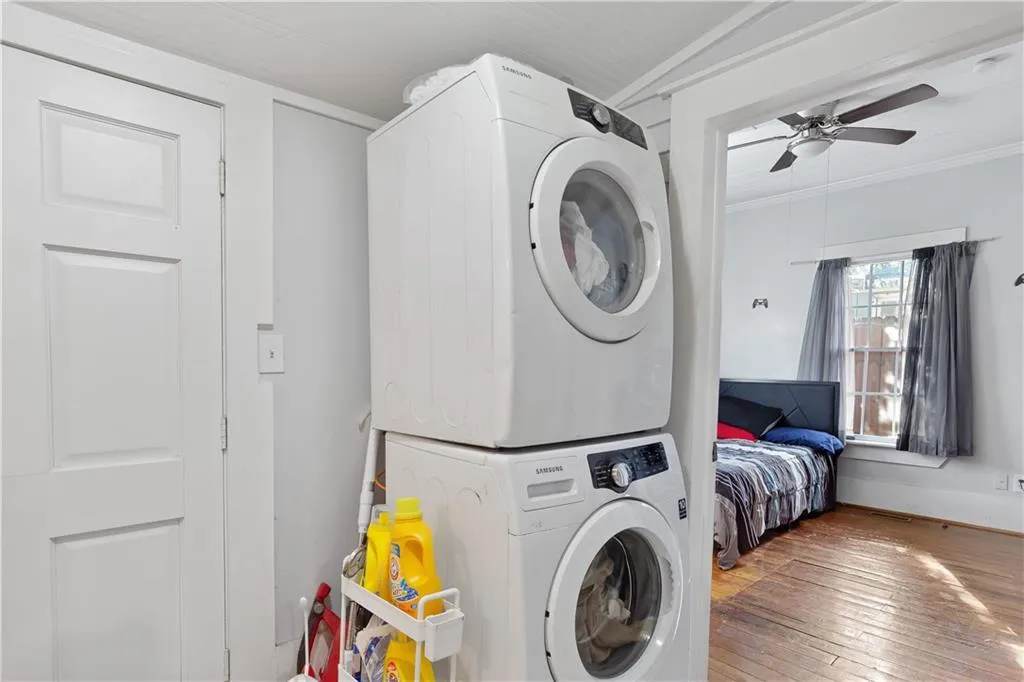 Laundry room with wood-type flooring, stacked washing maching and dryer, crown molding, and ceiling fan