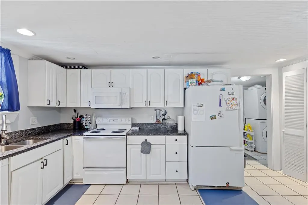 Kitchen featuring sink, white appliances, light tile floors, and white cabinetry
