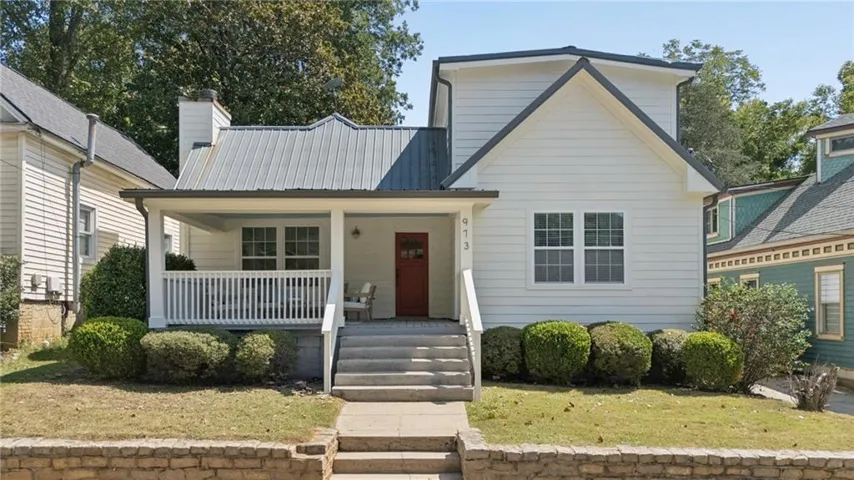 White siding exterior with a metal roof, covered front porch, concrete steps, and a red front door