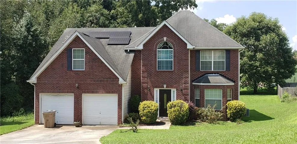 View of front of home featuring driveway, roof mounted solar panels, brick siding, a front lawn, and an attached garage