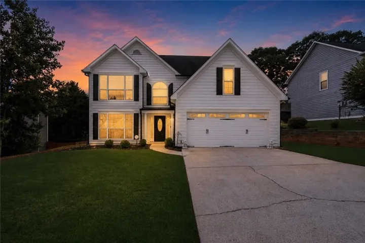 White siding exterior featuring a two-car garage, manicured lawn, an arched front door, and multiple large windows with black shutters