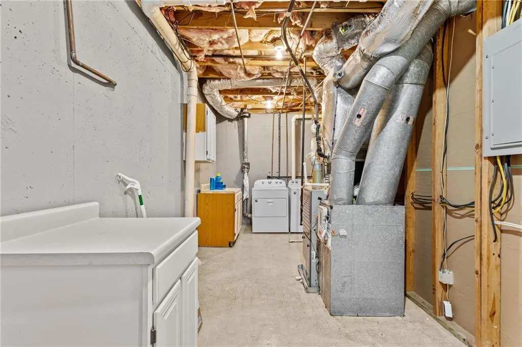 Unfinished below grade area featuring electric panel, heating unit, and independent washer and dryer