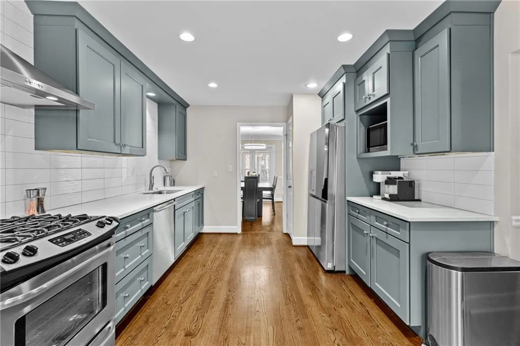 Kitchen featuring stainless steel appliances, decorative backsplash, light stone countertops, dark wood finished floors, and gray cabinets