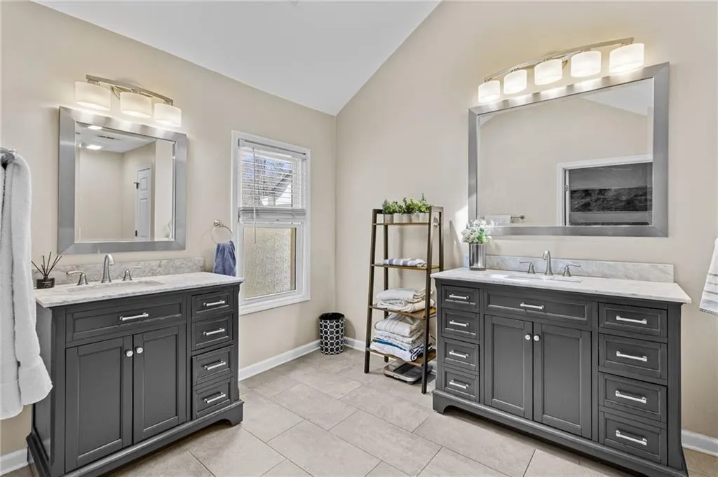 Full bath featuring lofted ceiling, two vanities, and light tile patterned floors