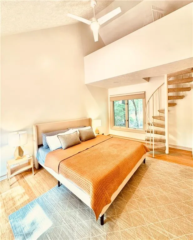 Bedroom with wood finished floors, a textured ceiling, a ceiling fan, and high vaulted ceiling