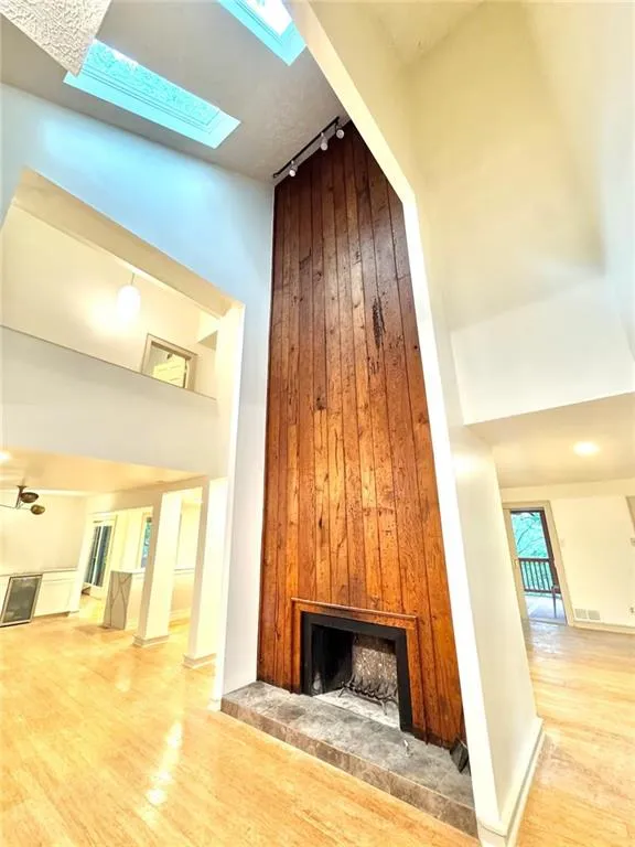 Unfurnished living room featuring a fireplace, track lighting, wood finished floors, a high ceiling, and wooden walls