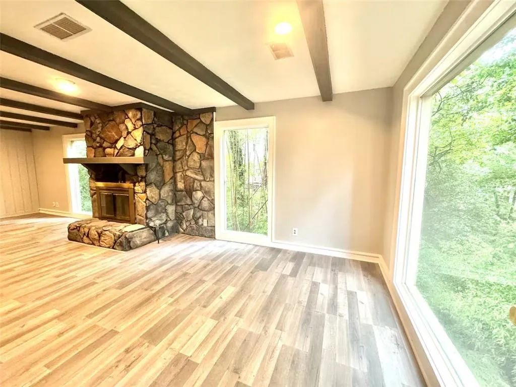 Unfurnished living room with wood finished floors, beamed ceiling, and a stone fireplace