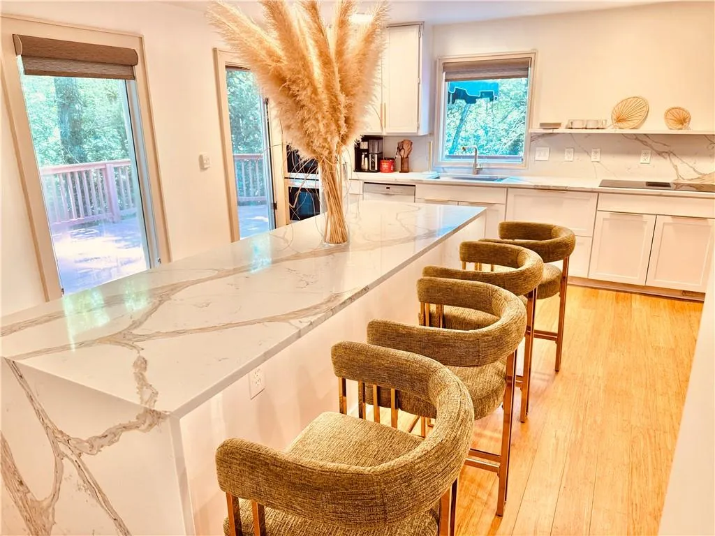 Kitchen featuring light wood-type flooring, white cabinetry, a breakfast bar area, and light stone counters