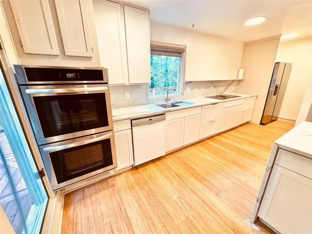 Kitchen featuring appliances with stainless steel finishes, light wood-type flooring, white cabinets, and light stone counters
