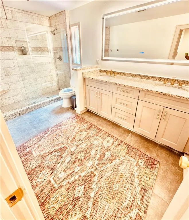 Full bath featuring a tile shower, double vanity, and tile patterned flooring