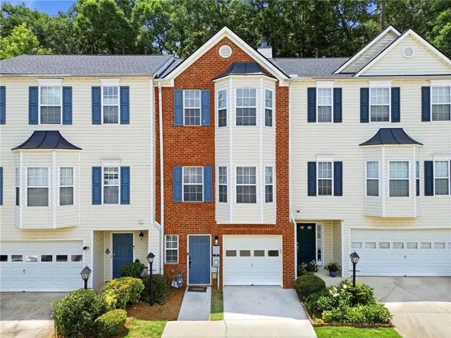 Three-story townhome with brick and siding exterior, featuring blue front doors, bay windows, and attached garages