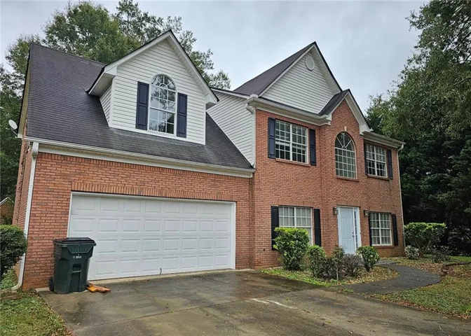 Brick facade residence featuring a two-car garage, white siding accents, and a light blue entry door