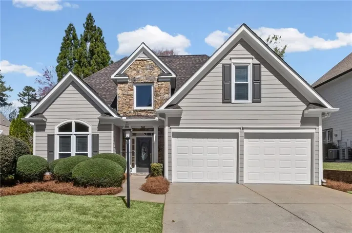 View of front facade featuring concrete driveway, stone siding, a front lawn, roof with shingles, and a garage