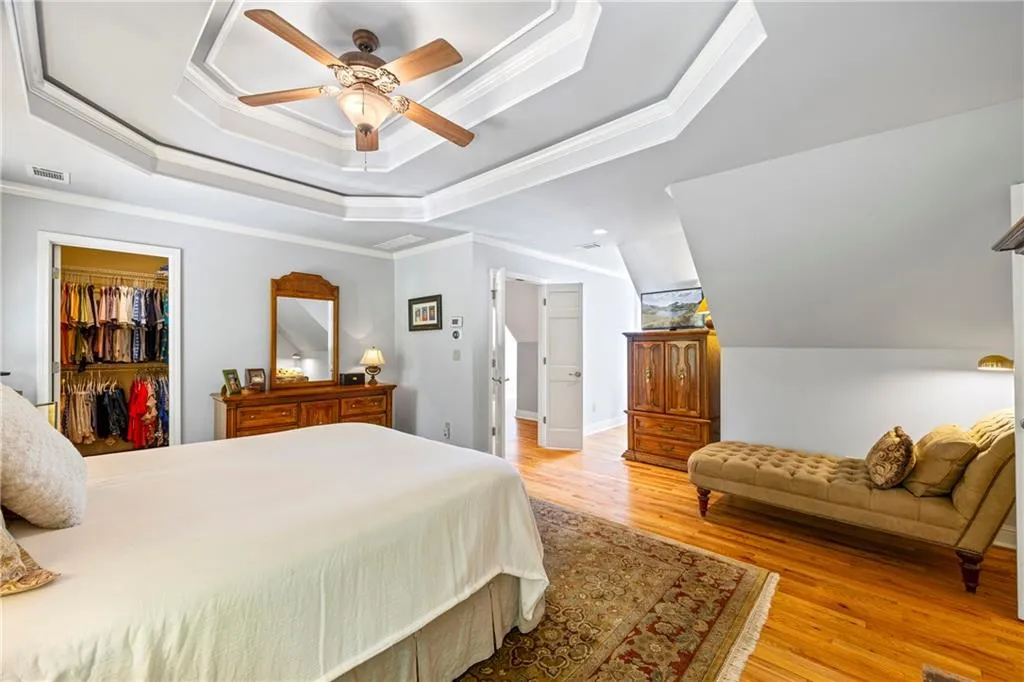 Bedroom featuring crown molding, a spacious closet, a tray ceiling, light wood-style flooring, and visible vents