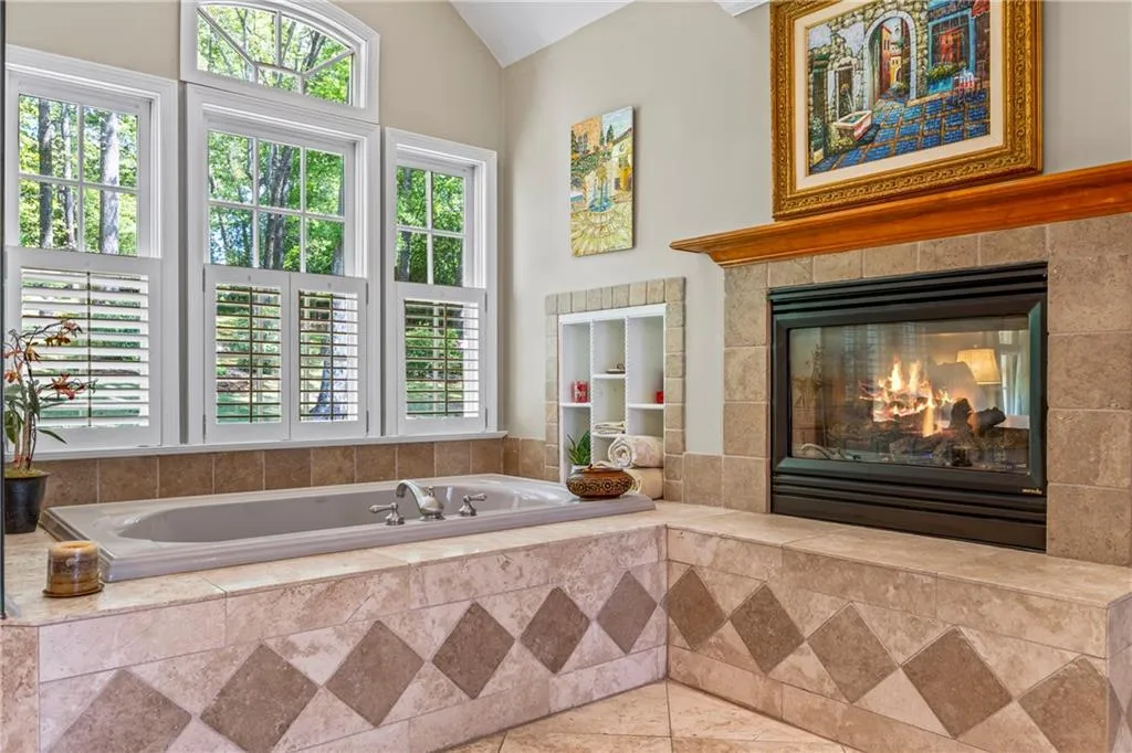 Bathroom featuring a tile fireplace, vaulted ceiling, and a garden tub