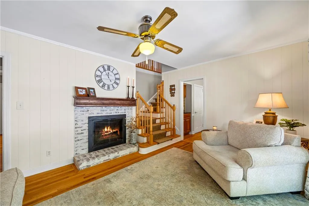 Living room featuring stairway, ornamental molding, a brick fireplace, and wood finished floors