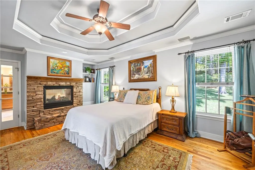 Bedroom with a tray ceiling, light wood-style floors, a fireplace, and ornamental molding