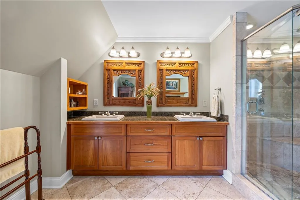 Bathroom featuring lofted ceiling, a sink, a shower stall, and double vanity