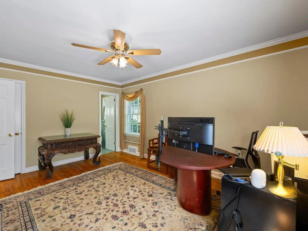 Office space featuring visible vents, baseboards, a ceiling fan, wood finished floors, and crown molding